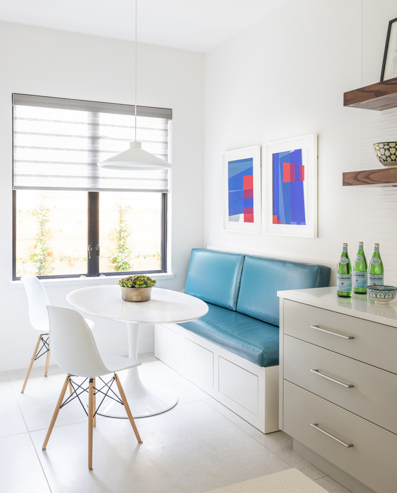 A bright breakfast nook with blue seating and two colorful artworks